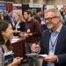 Students speaking with a professor at a crowded Postgraduate Study Fair, discussing graduate programs and funding opportunities in a vibrant academic exhibition hall.