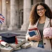 PhD student in the UK holding a piggy bank and academic books in front of a university building, symbolizing funding a doctorate with the UK doctoral loan and financial planning for international students
